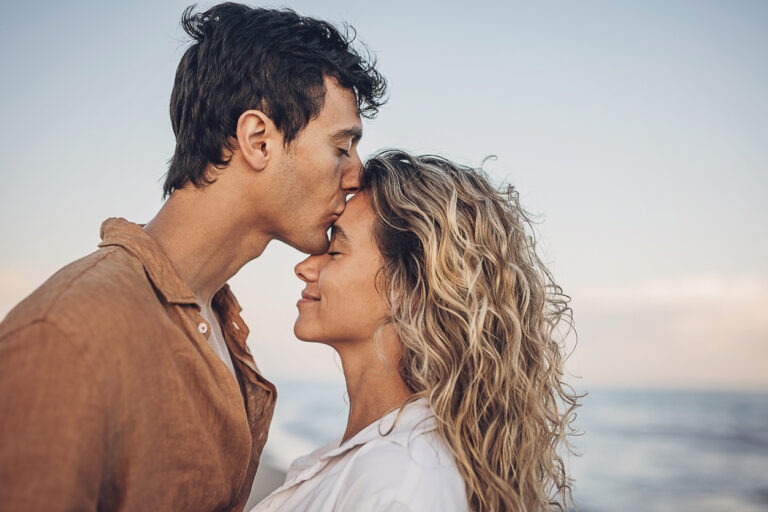 Romantic picture of a man kissing a woman on the forehead at the beach.